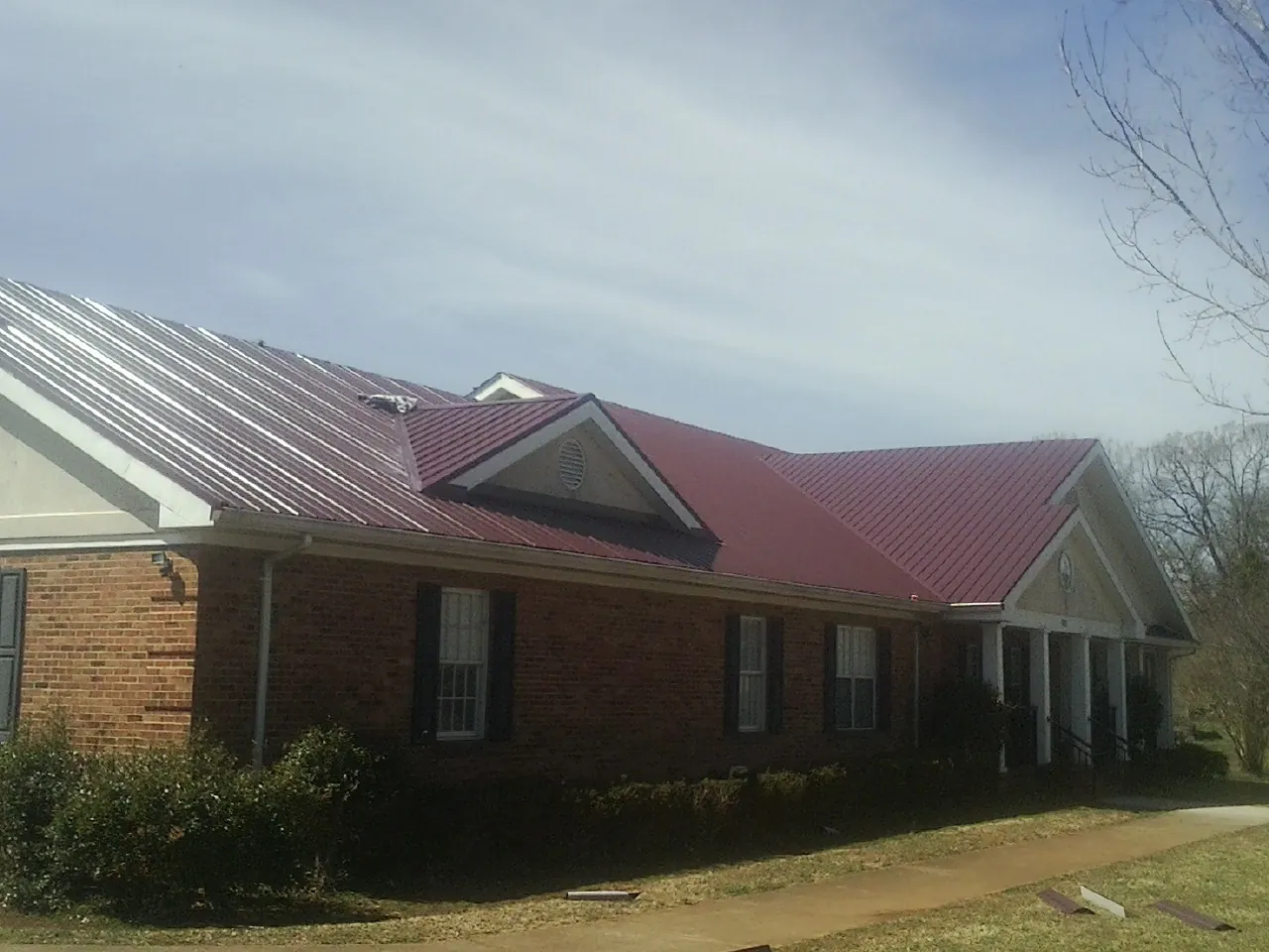 Red metal roof with gabled entries on a long brick building, from a Hail Damage Roof Repair job in Waynesburg