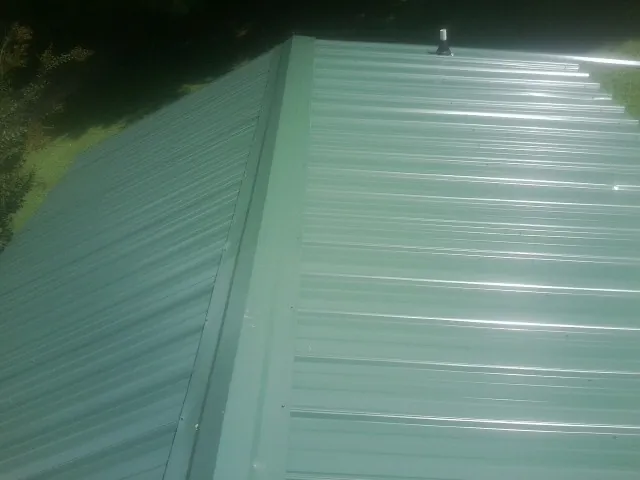 New green metal panels meeting at the ridge of a roof — Flat Roof Repair work by our crew in Waynesburg