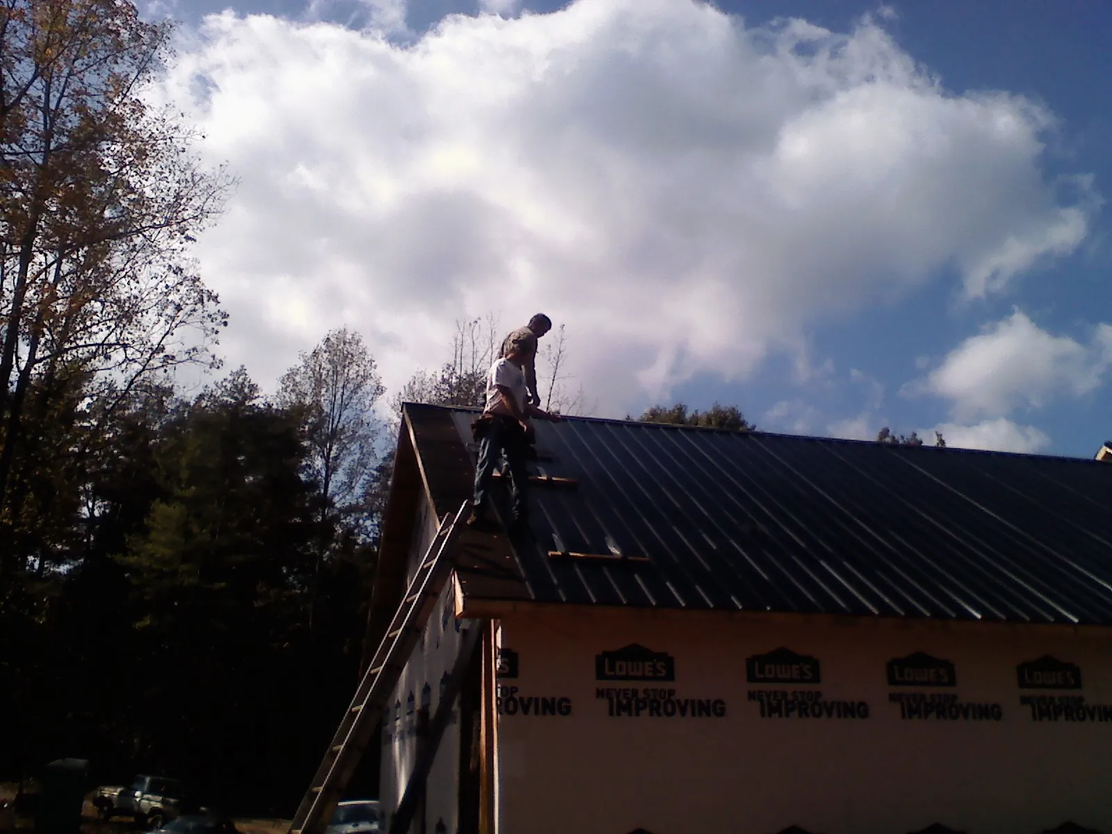 Roofer fastening dark metal panels high against a cloudy sky, from a Roof Inspection job in Waynesburg