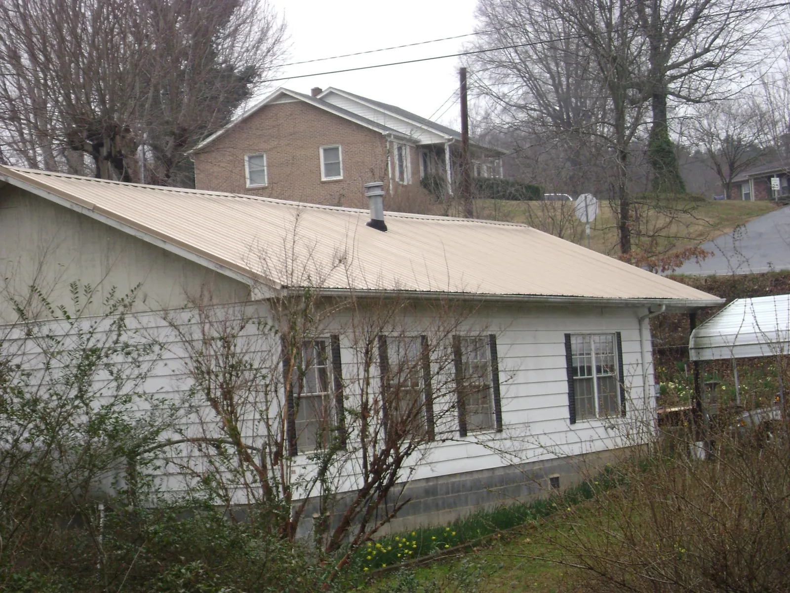 Tan metal roof on a white sided house set into a hillside — Commercial Roofing by Roofing Brothers in Waynesburg